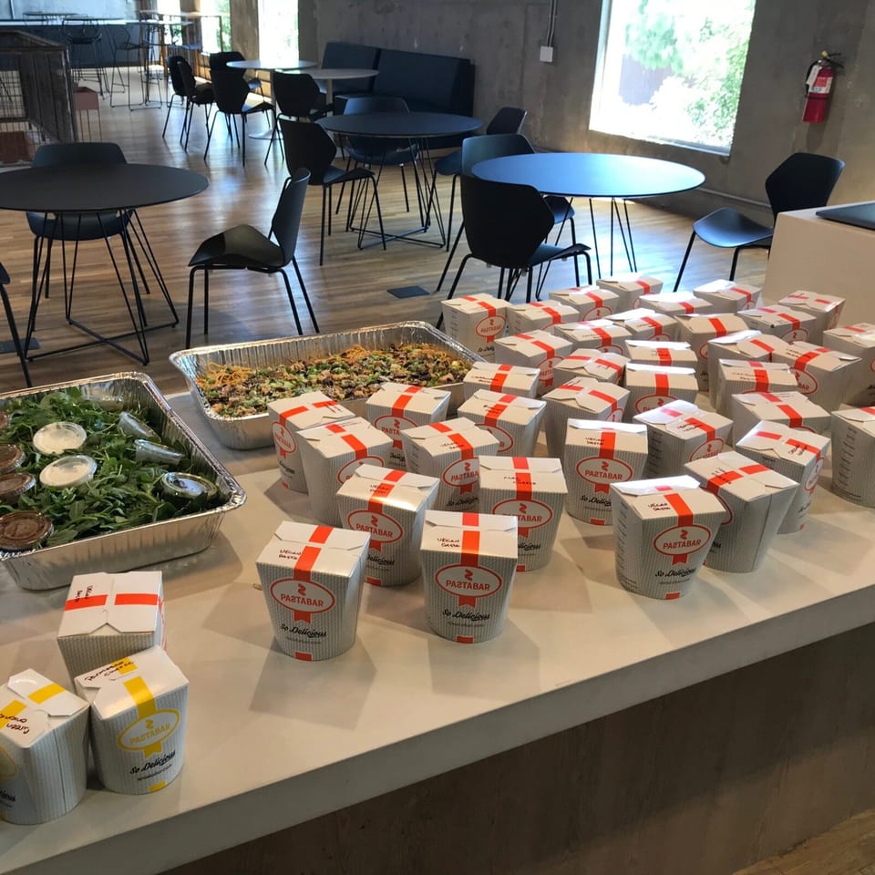 Catering spread of Pātābar takeaway boxes, noodles, salad, and sauces on a counter in a modern dining room.