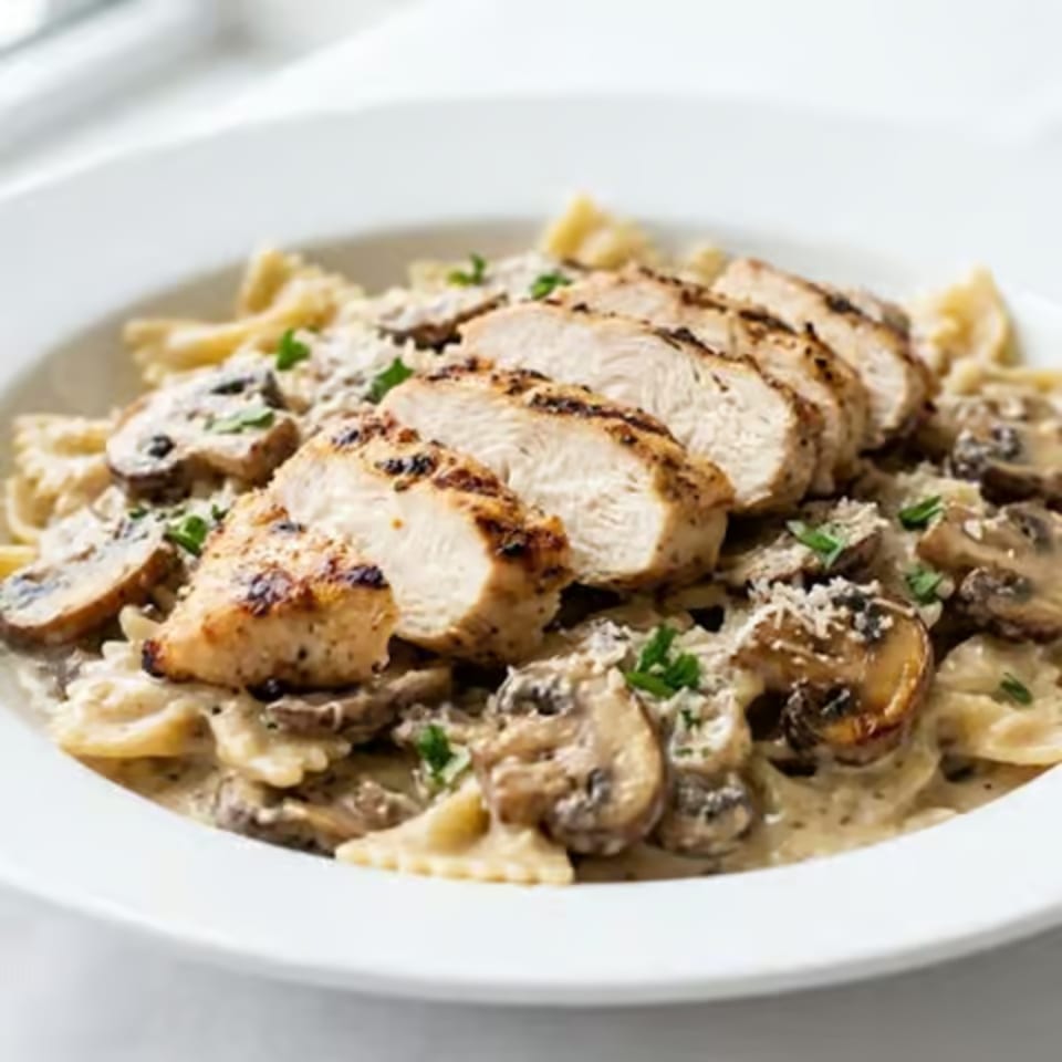 Sliced grilled chicken breast served over fries with creamy sauce, herbs, and cracked black pepper on a white plate.